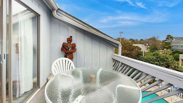 A balcony with a glass table and chairs, a statue, and a view of the neighborhood. - The Arbor Unit 303 Condo (Myrtle Beach)