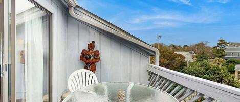 Un balcón con una mesa y sillas de vidrio, una estatua y vistas del barrio.
