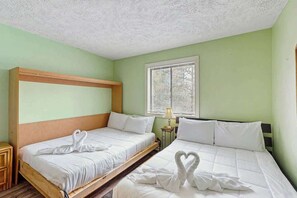 Ein Zimmer mit zwei Betten, jeweils mit weißer Bettwäsche und herzförmigen Verzierungen, einem Fenster mit Jalousien und einem Holzkopfende.