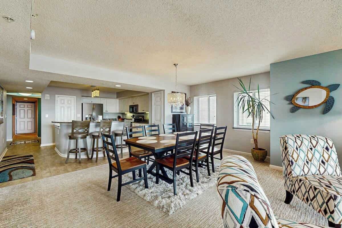 A spacious living area with a dining table, chairs, a sofa, and a kitchen in the background.