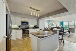 A modern kitchen with white cabinets, a central island, and a dining area with a view. - Yacht Club Villas 1-501 (North Myrtle Beach)
