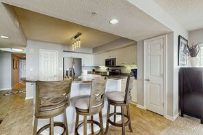 Una cocina moderna con armarios blancos, una isla central con taburetes y un refrigerador negro.