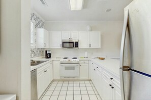 A compact kitchen with white cabinets, a microwave, an oven, and a refrigerator. - Coastal Retreat at Magnolia Place (Myrtle Beach)