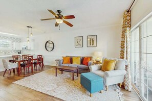 Ein Wohnzimmer mit einer Couch, einem Couchtisch und Sesseln, einem Deckenventilator und einem Essbereich mit Tisch und Stühlen.