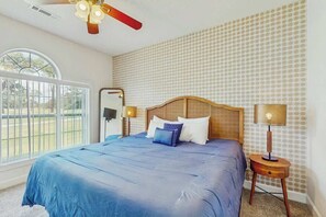 A bedroom with a large bed, a ceiling fan, a window, and a patterned wall. - Coastal Retreat at Magnolia Place (Myrtle Beach)