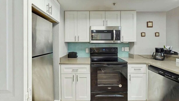 Een moderne keuken met witte kasten, een roestvrijstalen magnetron, een zwarte oven en een vaatwasser.