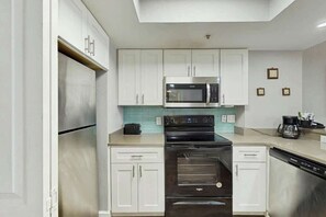 A modern kitchen with white cabinets, a stainless steel microwave, a black oven, and a dishwasher. - Compass Cove Unit 824 (Myrtle Beach)