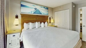 Een hotelkamer met een groot bed, een houten hoofdeinde, een schilderij boven het bed, twee bedlampen, een nachtkastje en een kledingkast.