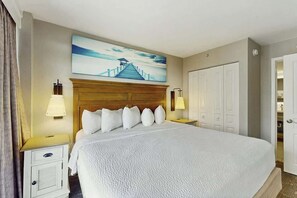 Ein Hotelzimmer mit einem großen Bett, einem Holz-Kopfteil, einem Gemälde darüber, zwei Nachttischlampen, einem Nachttisch und einem Kleiderschrank.