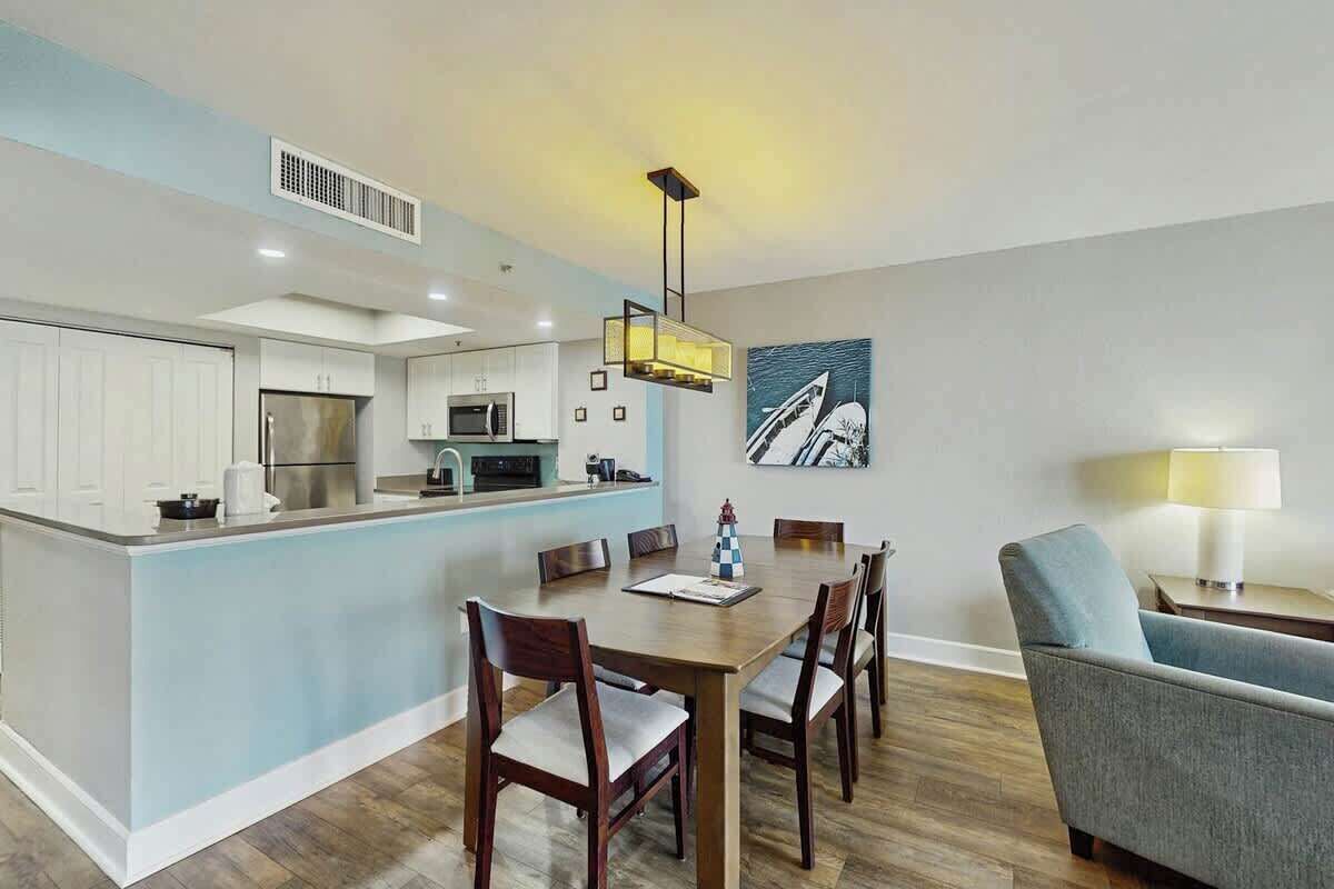A modern kitchen with white cabinets, a central island, and a dining area with a wooden table and chairs.