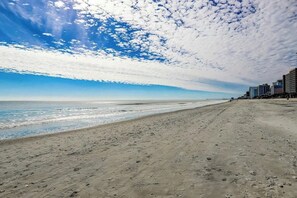 Ein Strand mit blauem Himmel und Gebäuden im Hintergrund.