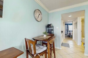 Ein Essbereich mit einem Holztisch und -stühlen, einer Wanduhr und einem durch einen offenen Durchgang einsehbaren Küchenbereich.