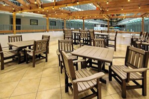 An indoor dining area with wooden tables and chairs, a tiled floor, and a ceiling with exposed beams and hanging lights. - Renaissance Luxe | Two Sixteen C (Myrtle Beach)