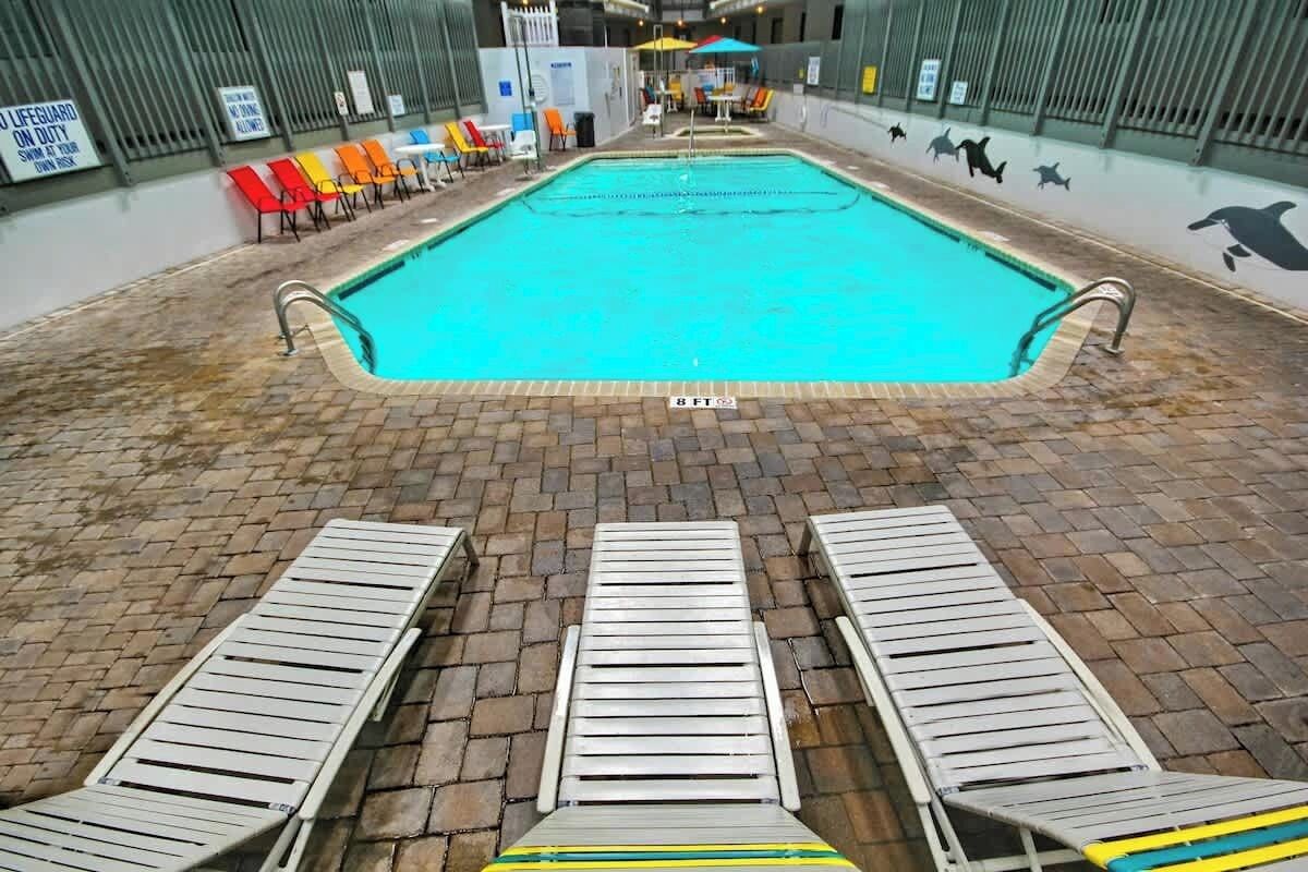 An indoor swimming pool with a tiled floor, a lifeguard on duty sign, and a dolphin mural on the wall.