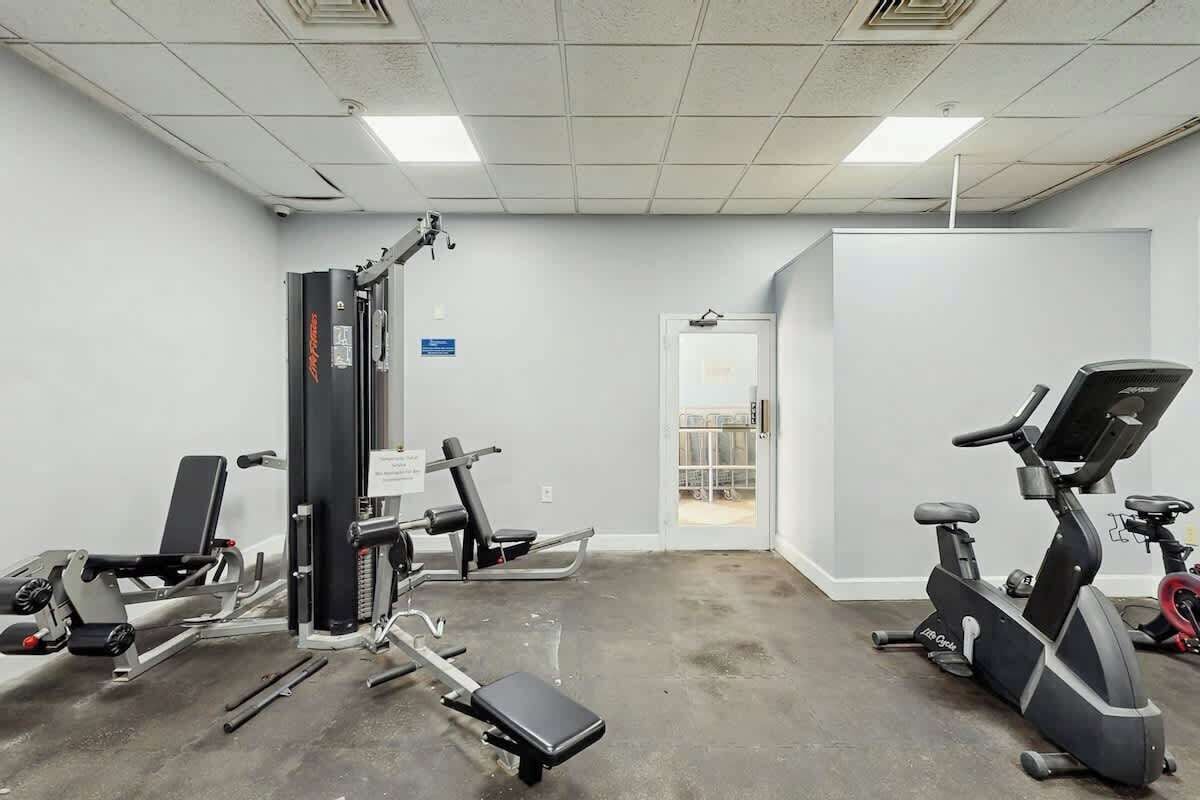 A gym with exercise equipment including a bench press, a leg press, and an elliptical machine.