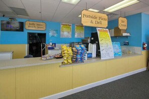 Ein Tresen mit Schildern für 'Portside Pizza & Deli' und 'Eis' in einem Geschäft mit blauer Wand und gelbem Tresen.