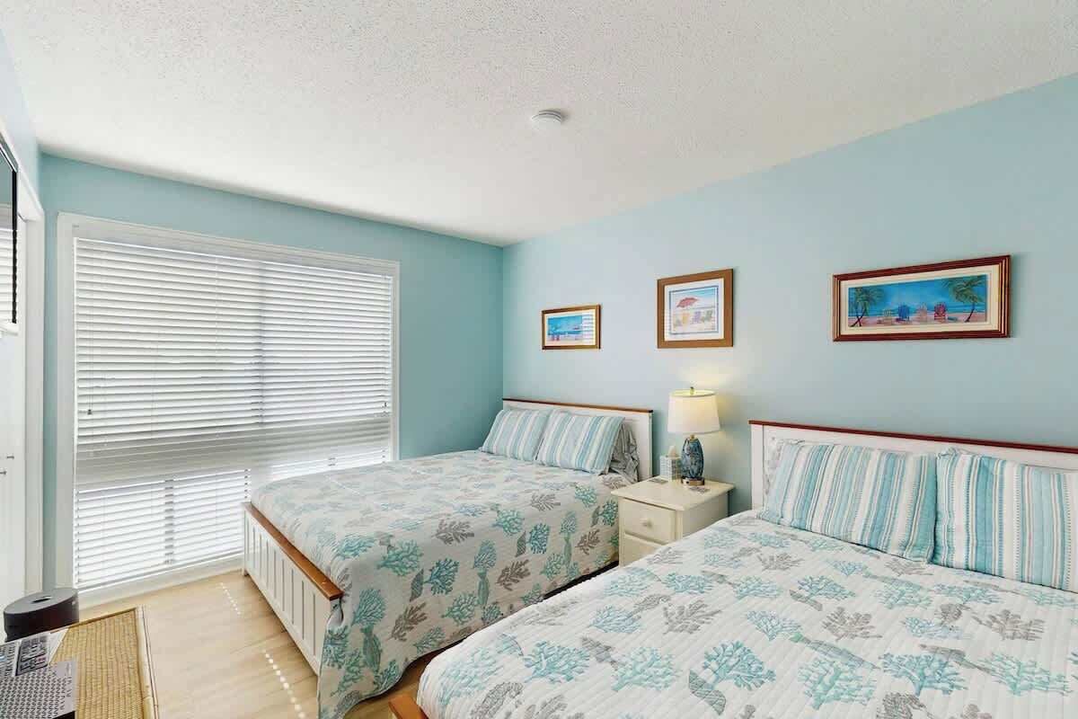 Une chambre avec deux lits, une fenêtre avec des stores et des tableaux accrochés au mur.