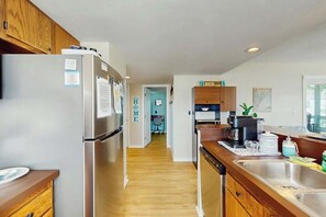 A modern kitchen with stainless steel appliances, wooden cabinets, and a central island with a sink. - Arcadian Dunes 04-213 (Myrtle Beach)