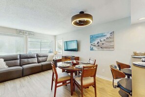 A modern living room with a sofa, dining table, chairs, and a TV. - Arcadian Dunes 04-213 (Myrtle Beach)