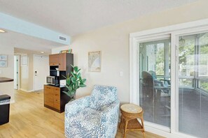 Un salon comprenant un canapé, une petite table, une plante et une porte-fenêtre coulissante donnant sur un espace extérieur.