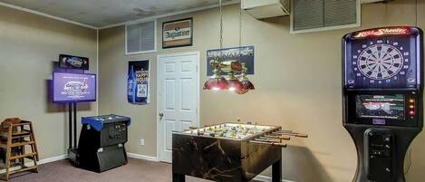 A room with a foosball table, a dartboard, and a television.