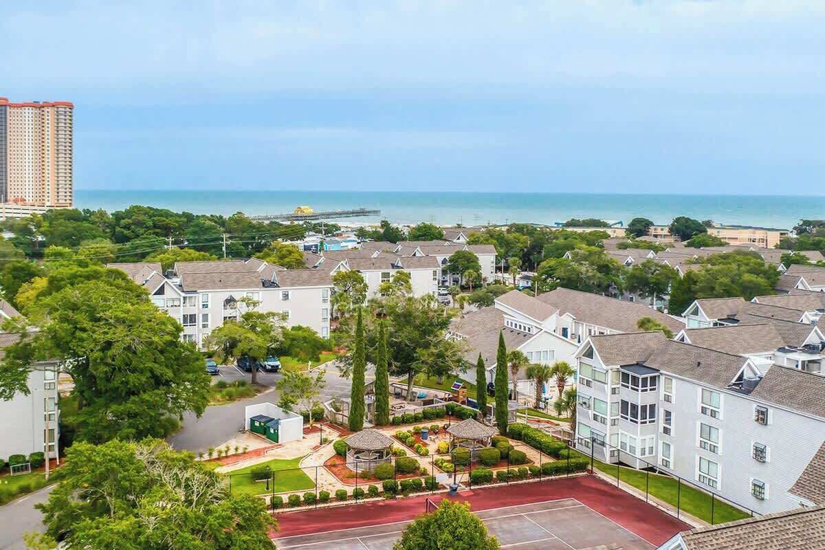 A residential area with multiple-story buildings, a paved road, and a view of the ocean.