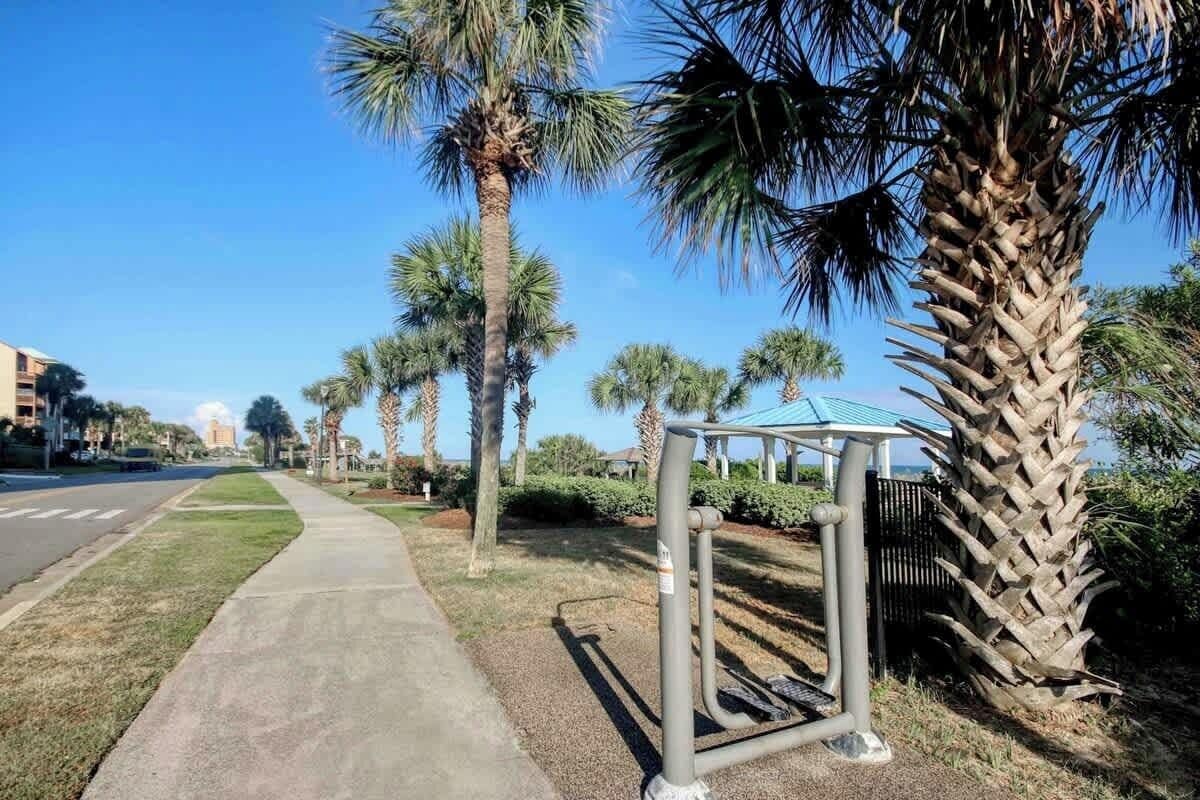 A sidewalk with palm trees, a covered structure, and a building in the background.