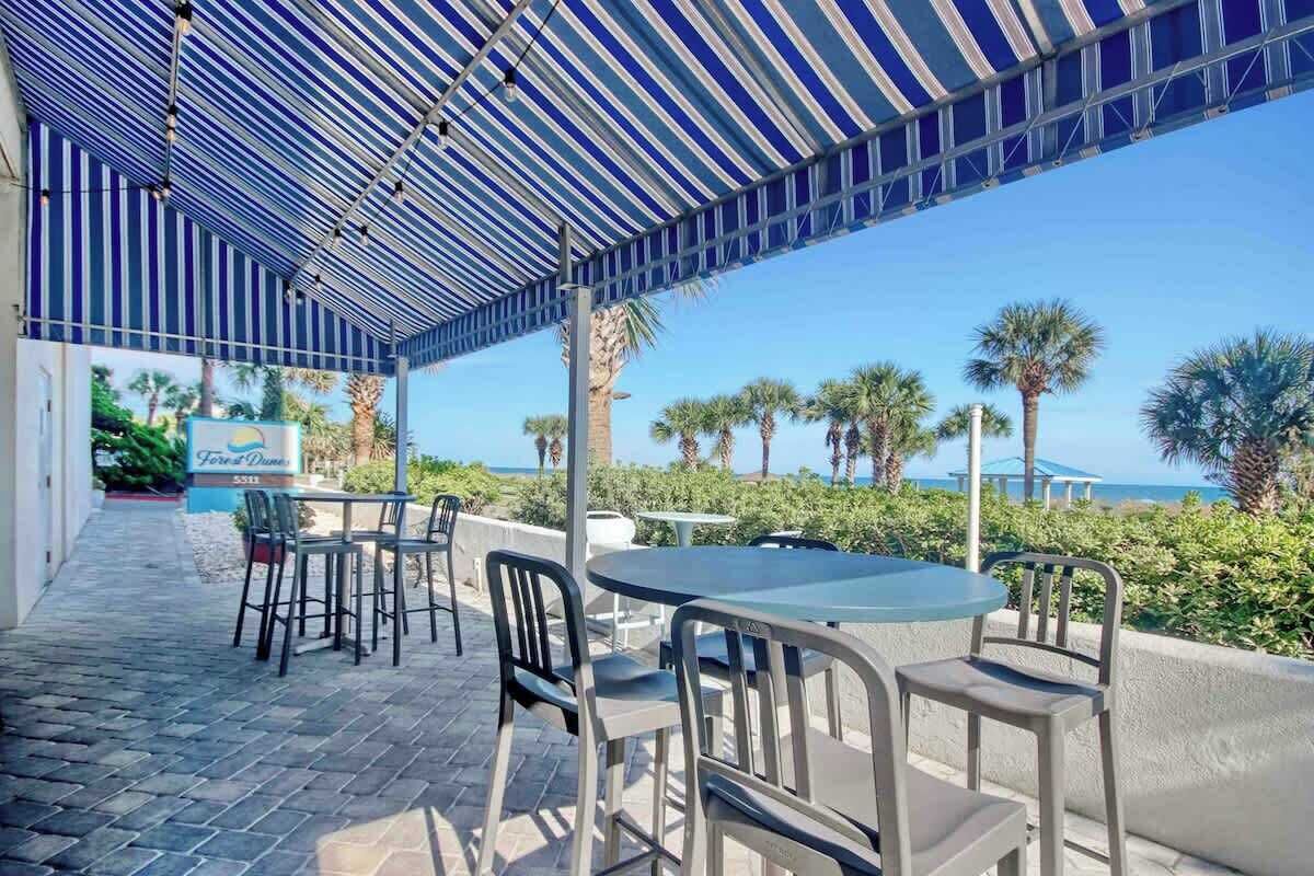 Une terrasse extérieure avec des tables et des chaises, offrant une vue sur une plage et des palmiers.