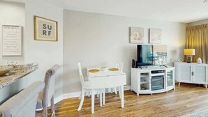 Ein modernes Wohnzimmer mit einem weißen Esstisch, weißen Stühlen, einem Flachbildfernseher und einem weißen Schrank.