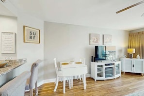Ein modernes Wohnzimmer mit einem weißen Esstisch, weißen Stühlen, einem Flachbildfernseher und einem weißen Schrank.