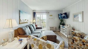 Ein Wohnzimmer mit einer Couch, einem Hocker, Sesseln, einem Fernseher und einem Fenster mit Blick.