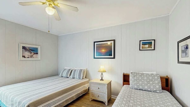 Ein Schlafzimmer mit zwei Betten, einem Deckenventilator, einem Nachttisch mit Lampe und gerahmten Bildern an der Wand.
