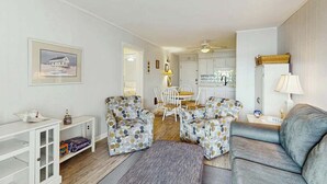 Ein Wohnzimmer mit einer Couch, zwei gemusterten Sesseln, einem Couchtisch und einem Essbereich mit Tisch und Stühlen.