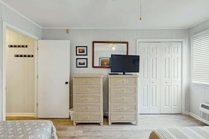 A room with a bed, a television on a stand, two wicker storage units, a wardrobe, and a mirror on the wall. - Ocean Boulevard Oasis (North Myrtle Beach)