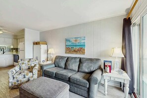 A living room with a sofa, armchair, and ottoman, a small table with a lamp, and a painting on the wall. - Ocean Boulevard Oasis (North Myrtle Beach)