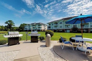 Eine Terrasse im Freien mit Grill, Sitzgelegenheit und Blick auf ein mehrstöckiges Gebäude.