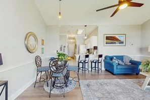 Ein modernes Wohnzimmer mit einem blauen Sofa, einem Essbereich mit gemusterten Stühlen und einem Deckenventilator.