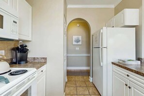 A kitchen with white cabinets, a stove, a microwave, and a refrigerator. - Magnolia Place at Myrtlewood (Myrtle Beach)