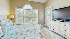 Quarto com cama, televisão, cômoda e janela com persianas.