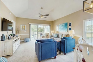 A spacious living room with a ceiling fan, a large window, and a dining area with a table and chairs. - Magnolia Place at Myrtlewood (Myrtle Beach)