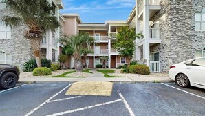 A multi-story residential building with a central courtyard, surrounded by greenery and palm trees.