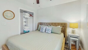 Une chambre à coucher comprenant un lit, un ventilateur de plafond, une table de chevet avec une lampe et une armoire.