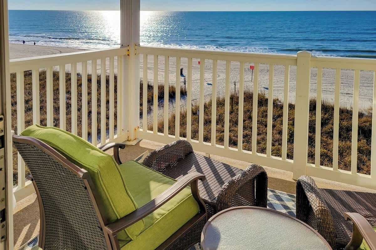 A balcony with wicker furniture overlooking a beach.