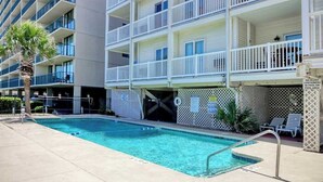 Une piscine située à côté d’un hôtel à plusieurs étages, doté de balcons.