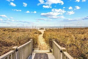Ein Holzsteg führt zu einem Strand unter blauem Himmel.