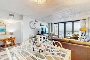 Ein modernes Wohnzimmer mit Glastisch, weißen Möbeln, einer Couch und einem Fernseher.