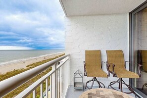 A balcony with a view of the beach, two wicker chairs, and a small table. - Coastal Luxe | Shoreham Six C (North Myrtle Beach)
