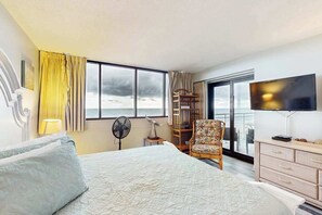 Une chambre d’hôtel avec un grand lit, une télévision, un fauteuil, une bibliothèque et une vue sur la mer.