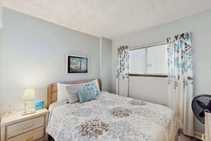 Ein Schlafzimmer mit einem Bett, einem Nachttisch, einer Lampe, einem Bild an der Wand und einem Fenster mit Vorhängen.