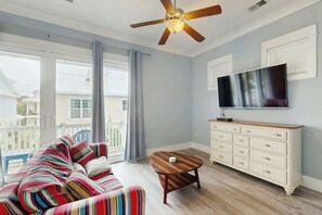 A living room with a sofa, a coffee table, a TV, and a ceiling fan. - Cloisters on the Ocean 326 (Myrtle Beach)